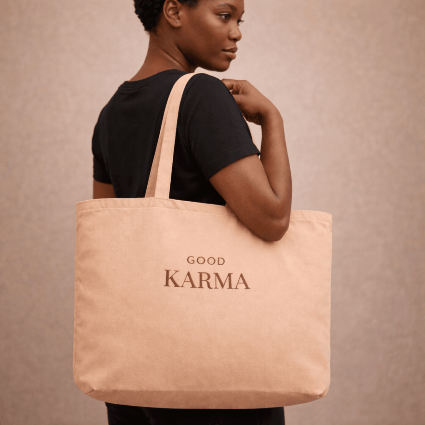 Person holding a beige tote bag with 'Good Karma' text on a beige background