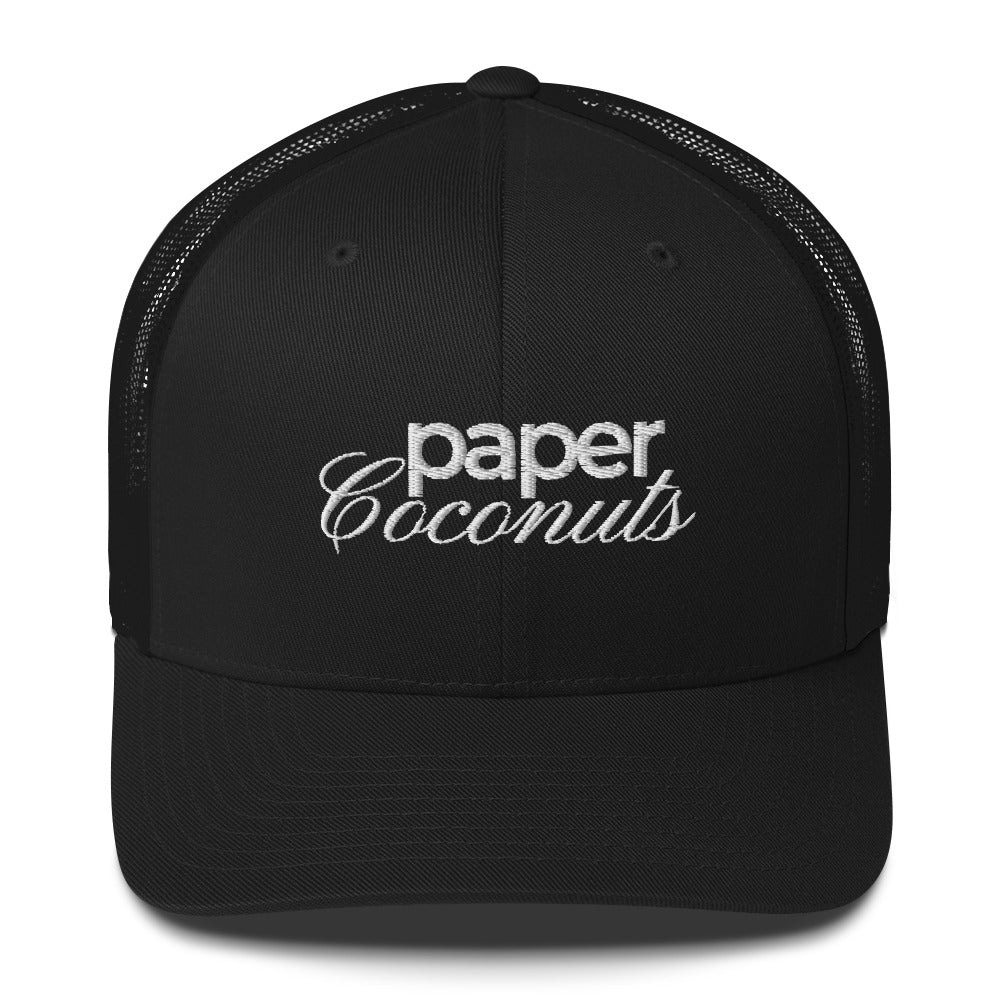 Black trucker hat with "Paper Coconuts" logo in stylized embroidered white text. The cap features a black front panel and white mesh back, showcasing a modern brand design .