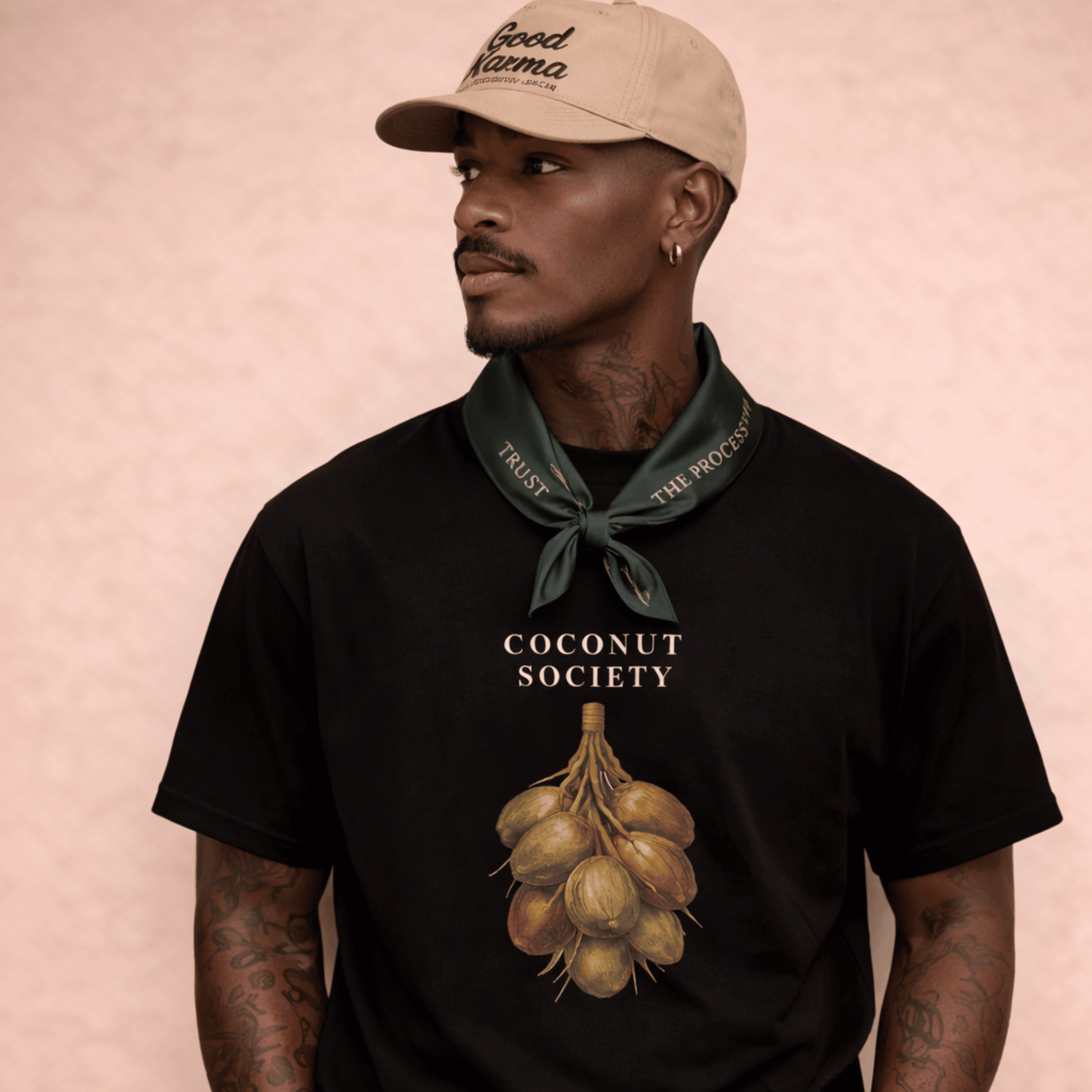 Man wearing a black t-shirt with 'Coconut Society' design and 'Good Mama' cap on a pink background