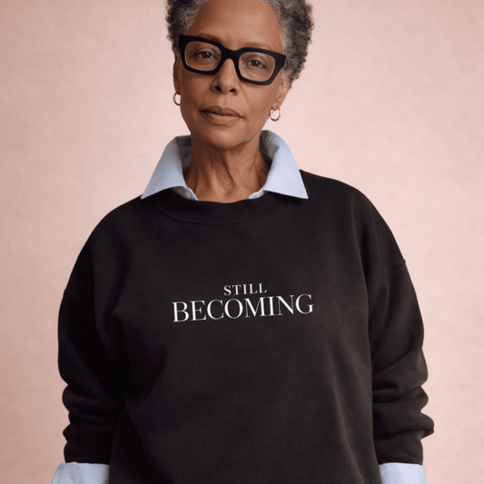Person wearing a black sweatshirt with 'STILL BECOMING' text on a pink background